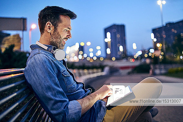 Mann benutzt Tabletten  während er abends in der Stadt auf einer Bank sitzt