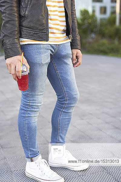 Auf dem Bürgersteig stehender Mann  der einen Plastikbecher mit rotem Erfrischungsgetränk hält  Teilansicht