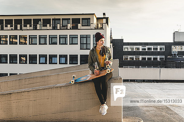 Stilvolle junge Frau mit Skateboard auf dem Parkdeck