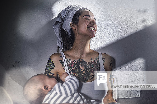 Glücklich tätowierte junge Frau hält ihr Baby zu Hause