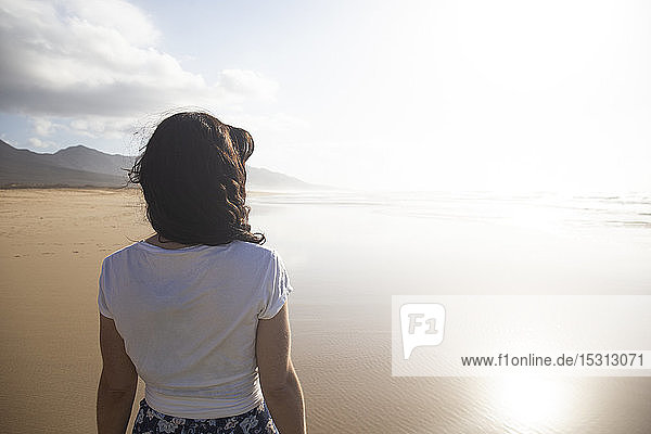 Rückenansicht einer Frau  die am Strand steht und auf das Meer schaut  Fuerteventura  Spanien