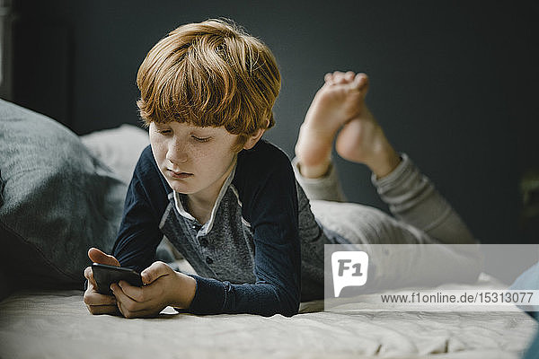 Porträt eines rothaarigen Jungen  der auf der Couch liegt und auf sein Handy schaut