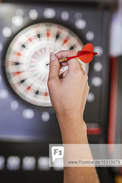 Close-up of woman's hand holding dart in front of dartboard