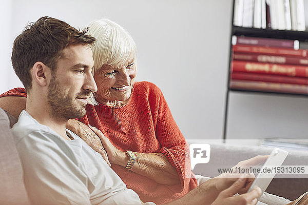 Enkel sitzt auf der Couch und benutzt ein digitales Tablet mit seiner Großmutter