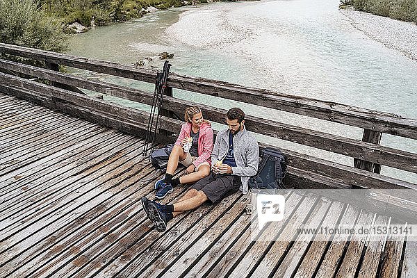 Junges Paar macht während einer Wanderung auf einer Holzbrücke eine Pause,  Vorderriss,  Bayern,  Deutschland
