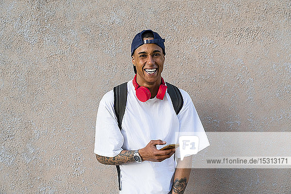 Porträt eines tätowierten jungen Mannes mit Smartphone und roten Kopfhörern