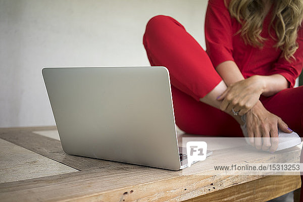 Close-up of woman with laptop sitting on wooden table at home