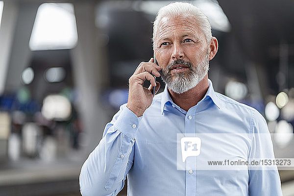 Ein reifer Geschäftsmann telefoniert am Bahnsteig mit einem Mobiltelefon