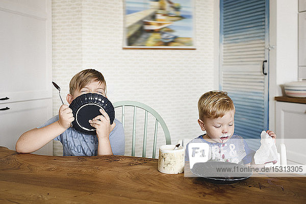 Two brothers with plates sitting at table at home