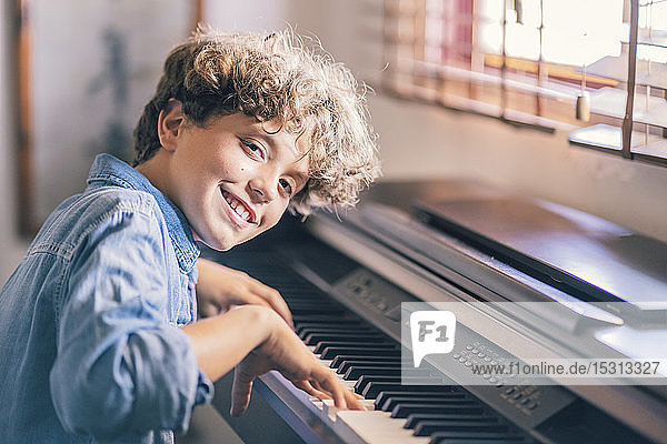 Porträt eines lächelnden Jungen  der zu Hause Klavier spielt