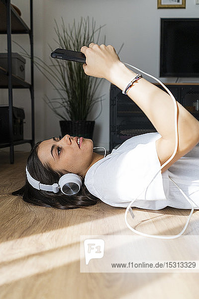 Junge Frau liegt mit Smartphone und Kopfhörern auf dem Boden