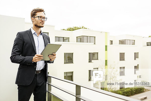 Businessman with tablet standing on balcony in a development area