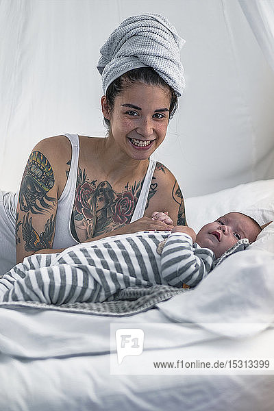Porträt einer lächelnden tätowierten jungen Frau mit ihrem Baby im Himmelbett