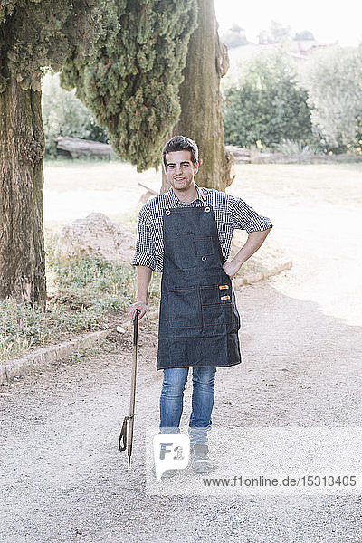 Porträt eines selbstbewussten Junglandwirts  der ein Werkzeug auf einem Feldweg hält