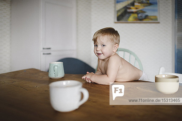 Portrait of shirtless little boy leaning on kitchen table
