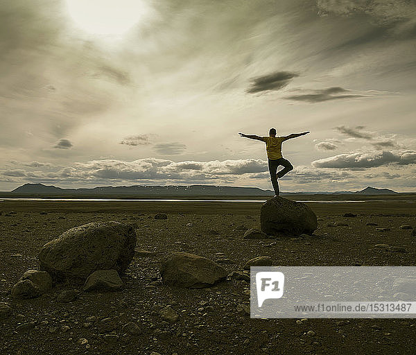 Reifer Mann balanciert auf einem Bein auf einem Felsen im vulkanischen Hochland von Island
