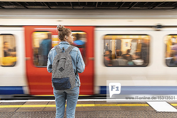 Rückansicht einer jungen Frau am U-Bahnhof mit einfahrendem Zug