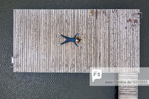 Luftaufnahme einer jungen Triathletin  die auf einem Steg an einem See liegt