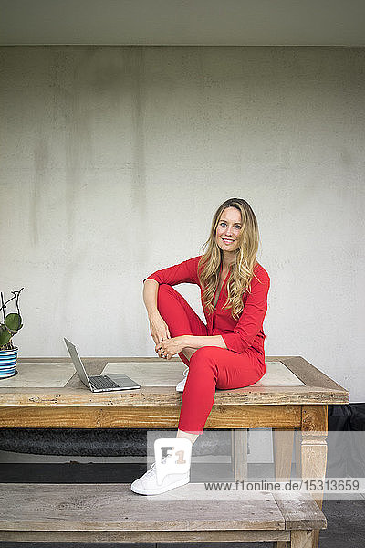 Lächelnde Frau mit Laptop  die zu Hause auf einem Holztisch sitzt