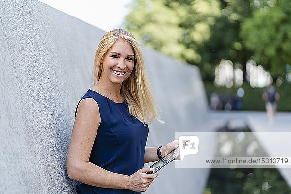 Porträt einer lächelnden blonden Geschäftsfrau mit digitalem Tablet im Freien