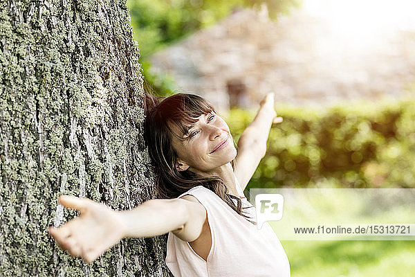 Bildnis einer lächelnden brünetten Frau  die an einen Baumstamm gelehnt ist