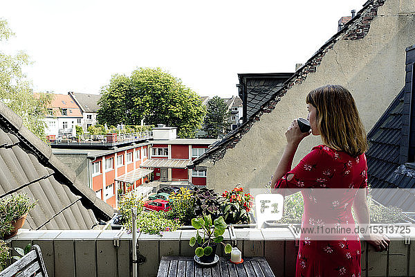 Junge Frau entspannt sich mit einer Tasse Kaffee auf dem Balkon und schaut in die Ferne