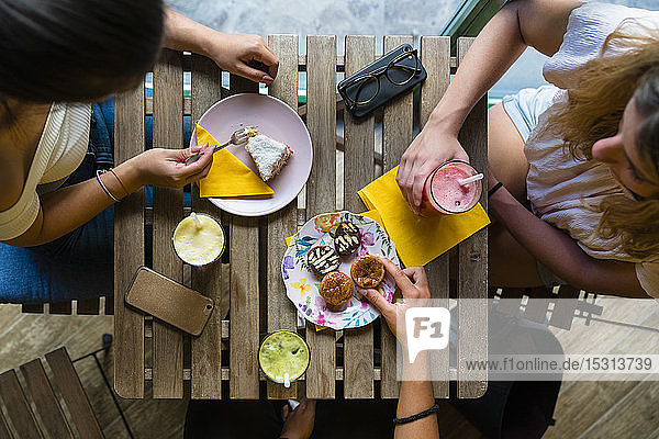 Draufsicht auf drei junge Frauen  die an einem Holztisch mit Smoothies und Keksen sitzen