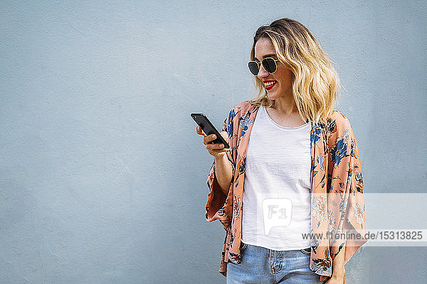 Lächelnde blonde Frau mit Smartphone  blauer Hintergrund