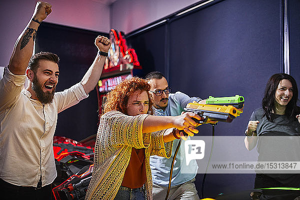 Glückliche Freunde spielen und schießen mit Pistolen in einer Spielhalle