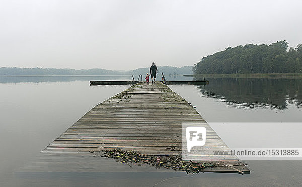 Father and a toddler daughter walking along boardwalk on a lake  Skane County  Sweden