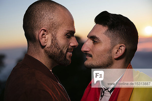 Gay couple with gay pride flag face to face at sunset
