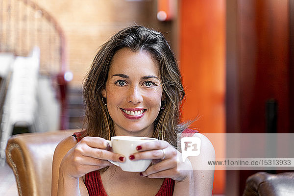 Porträt einer lächelnden jungen Frau mit Tasse Kaffee