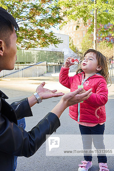 Vater und kleine Tochter spielen im Freien mit Seifenblasen