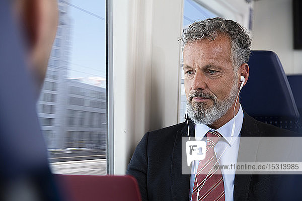 Mature businessman sitting train  using earphones