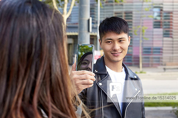Smiling young man taking a cell phone picture of woman in Barcelona  Spain