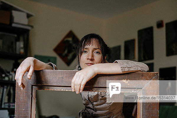 Porträt einer Malerin in ihrem Atelier auf einem Bilderrahmen lehnend