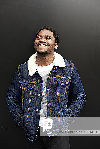 Portrait of laughing man wearing denim jacket standing in front of dark background looking up