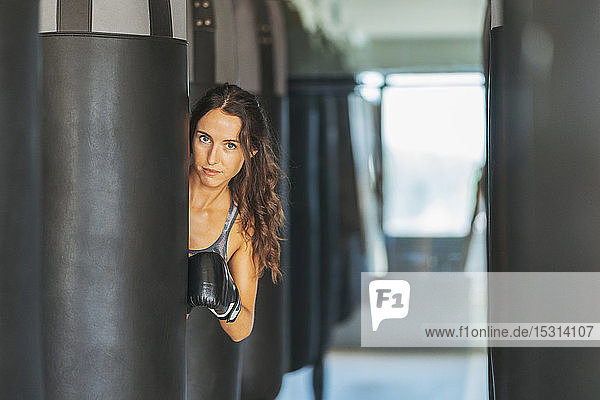 Portrait of woman with boxing gloves behind sandbag in gym
