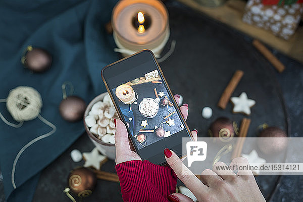 Woman's hand taking picture of cup of Hot Chocolate with marshmellows with smartphone