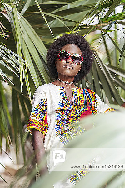 Coole junge Frau mit Sonnenbrille posiert zwischen tropischen Pflanzen