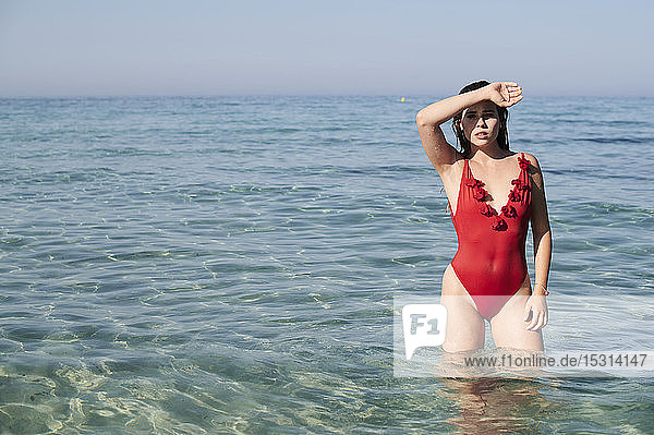 Junge Frau im roten Badeanzug steht im Meer