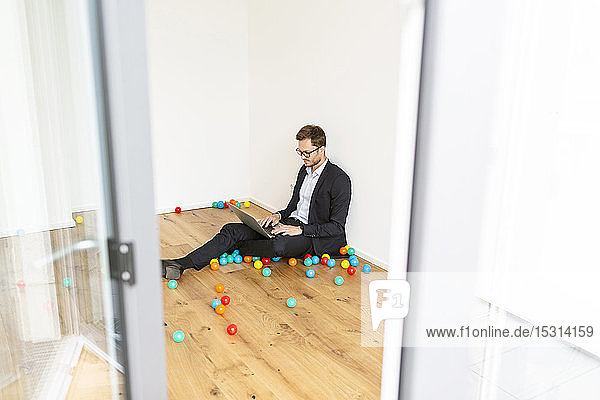 Businessman sitting on the floor using laptop surrounded by colourful balls