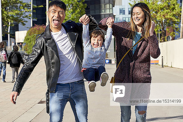 Happy parents holding hands of little girl while jumping  Barcelona  Spain