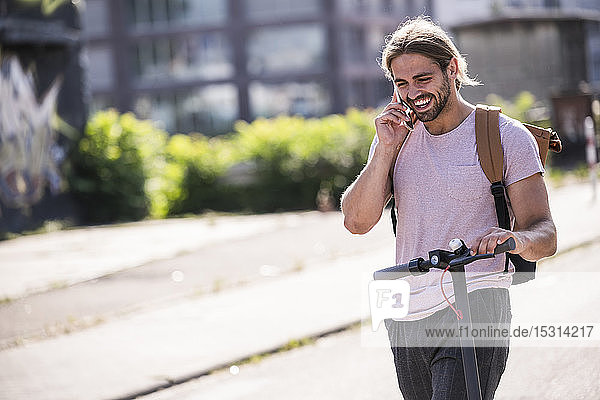 Happy young man with electric scooter talking on the phone on the street