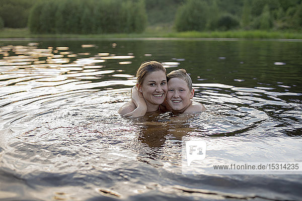 Porträt einer glücklichen Mutter und eines Sohnes  die bei Sonnenuntergang in einem See baden