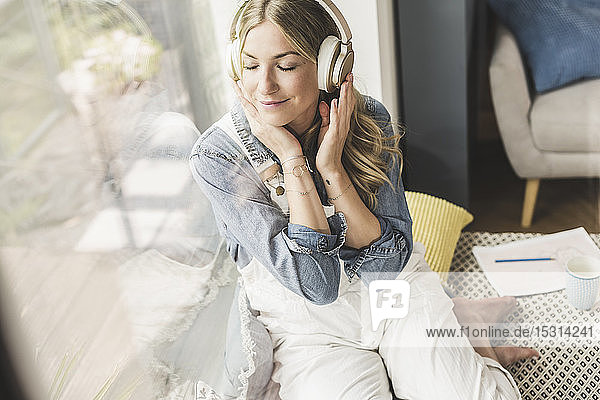 Frau sitzt zu Hause am Fenster und hört Musik mit Kopfhörern