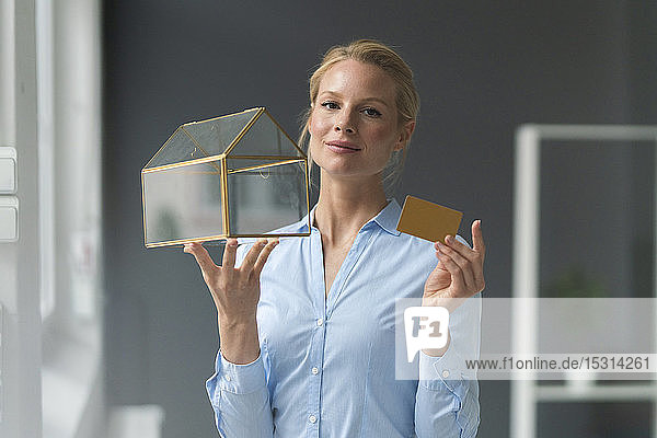 Lächelnde junge Geschäftsfrau mit Glashausmodell und Kreditkarte