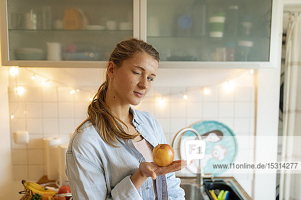 Portrait of young woman holding an apple at home
