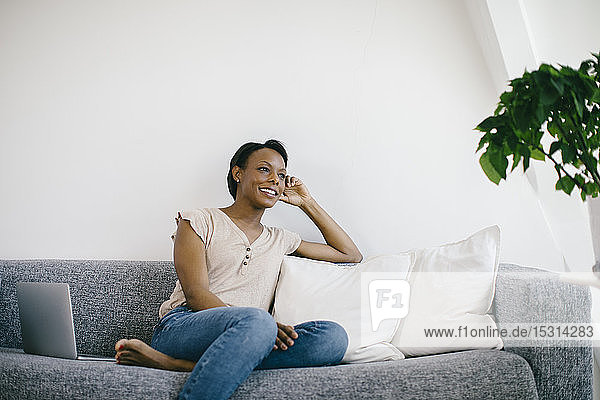 Smiling woman sitting on couch at home with laptop