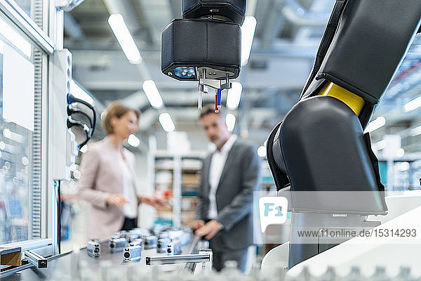 Roboter in einer modernen Fabrikhalle mit einem Geschäftsmann und einer Geschäftsfrau im Hintergrund